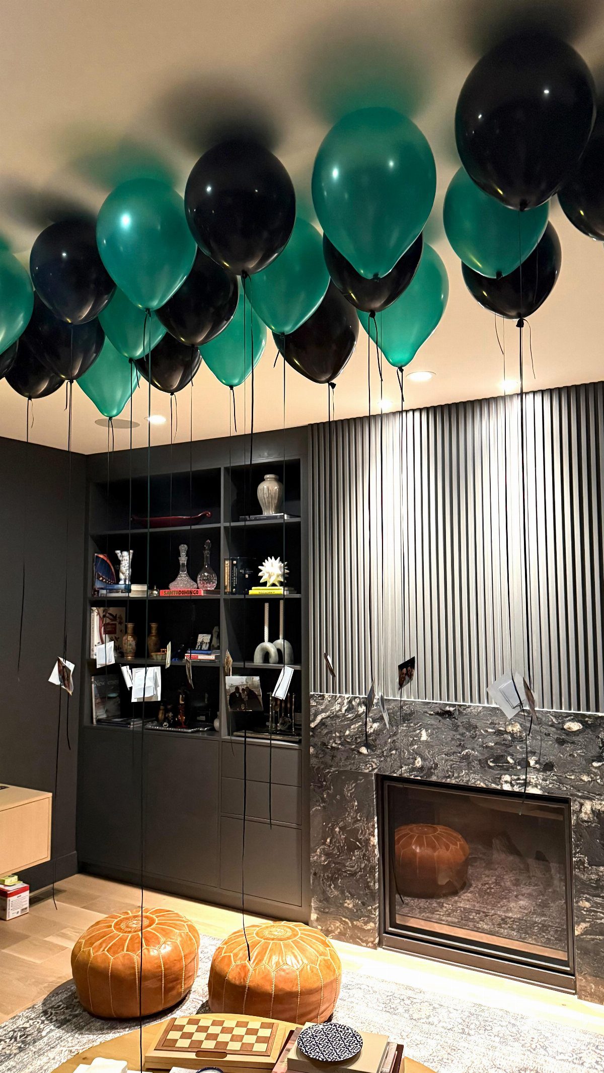 Teal and black balloons floating against a ceiling with strings hanging down in a living room.