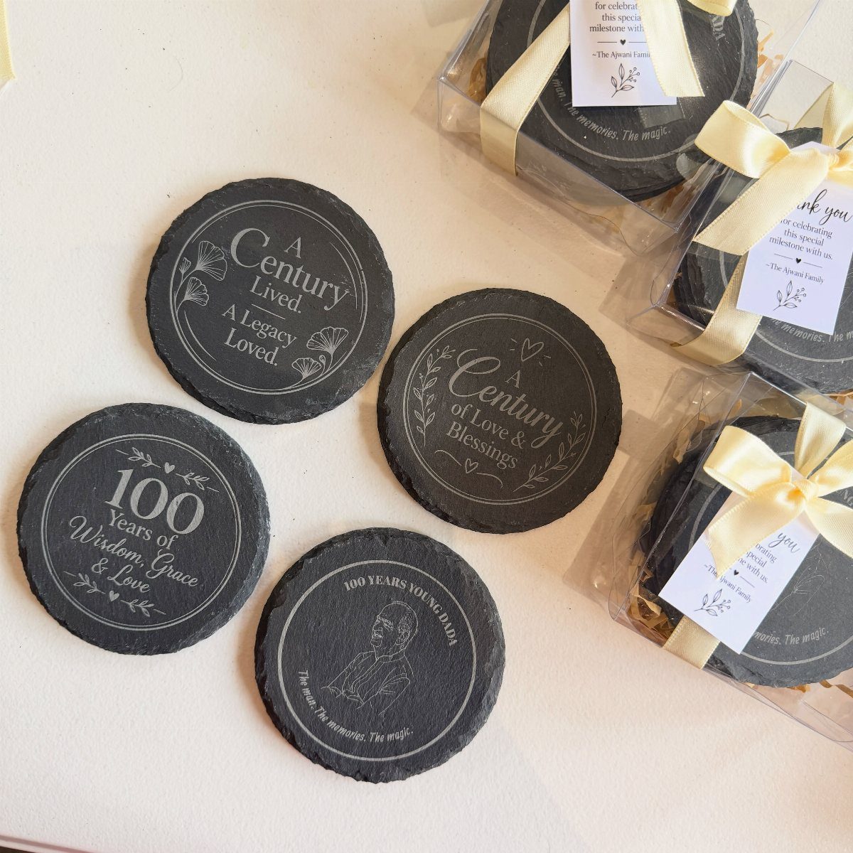 Black slate coasters with engraved text and cream ribbons arranged on a white surface.