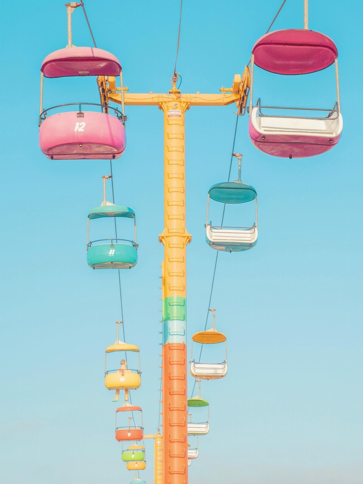 Colorful gondolas hang from a tall yellow amusement park ride against a blue sky.