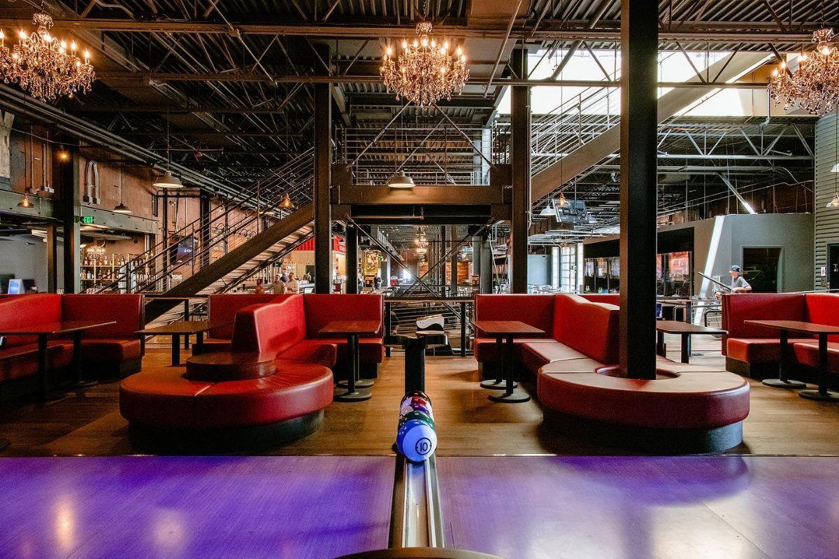 Bowling ball on a return track overlooking a modern lounge with red booths and chandeliers.