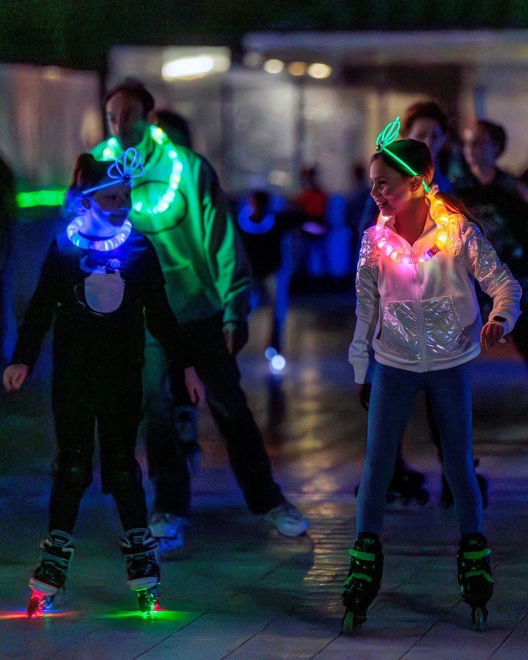 Two girls roller skating at night wearing glowing neon necklaces and bracelets.