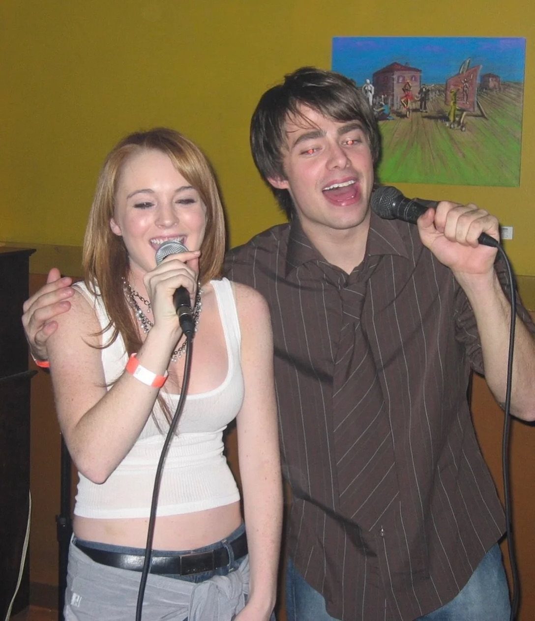 A young woman and man singing joyfully into handheld microphones indoors.