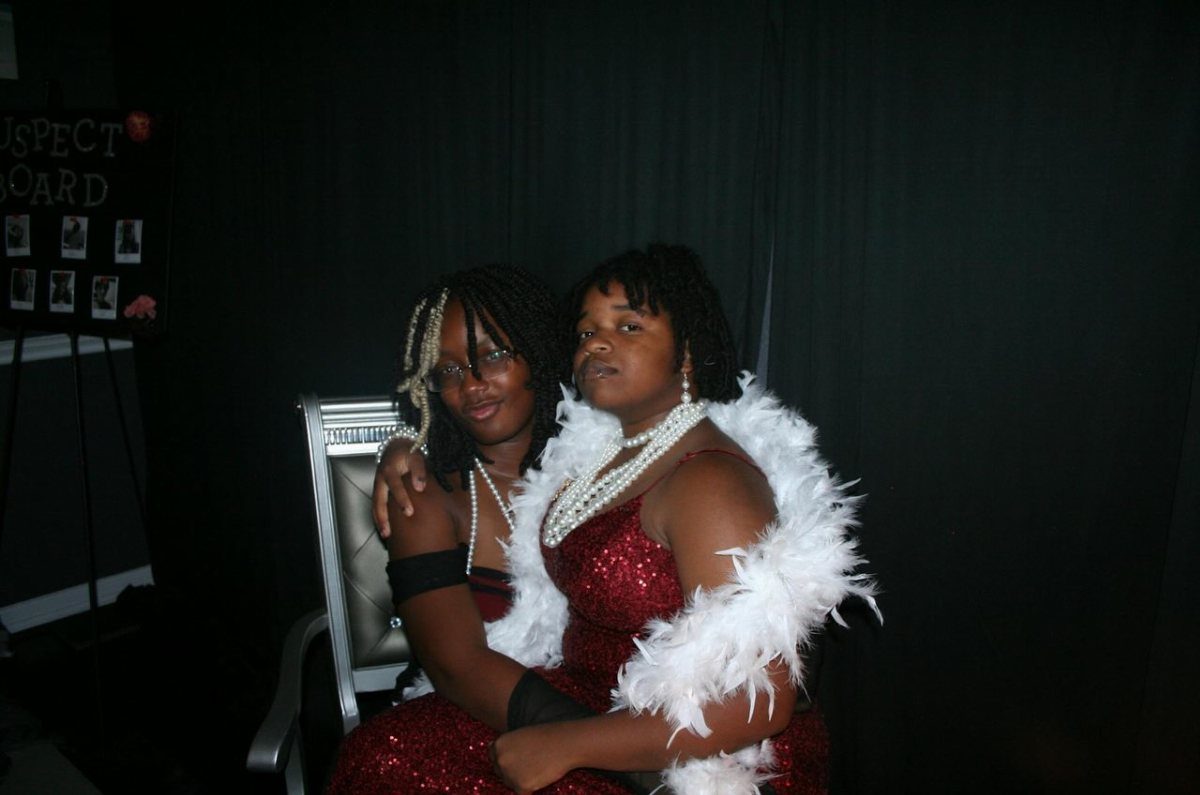 Two young women in red sequin dresses and white feather boas posing together.