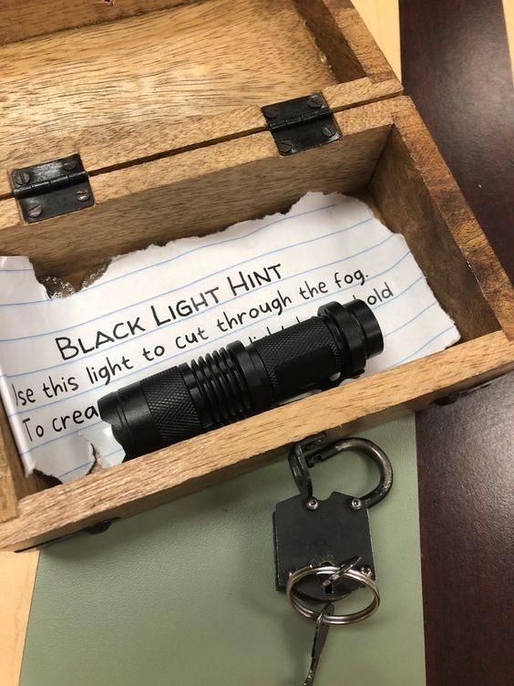 A wooden box containing a black flashlight and a handwritten hint on lined paper.