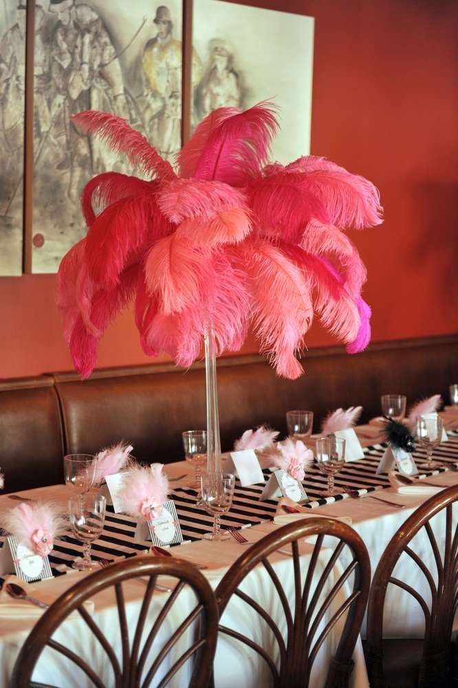 A long dining table decorated with large pink feather centerpieces and elegant glassware.