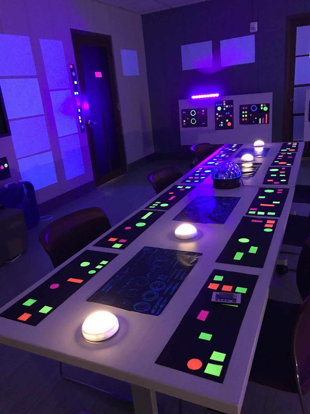 A long table with glowing neon patterns and white light orbs in a purple room.