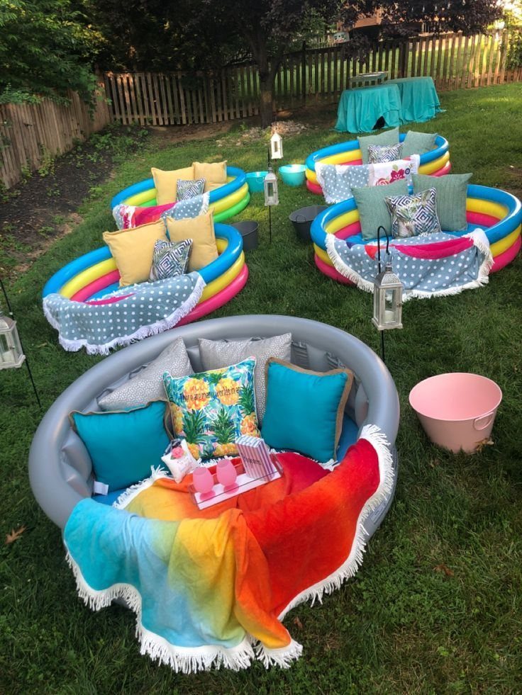 Inflatable pools filled with colorful pillows and blankets arranged on a green lawn outdoors.