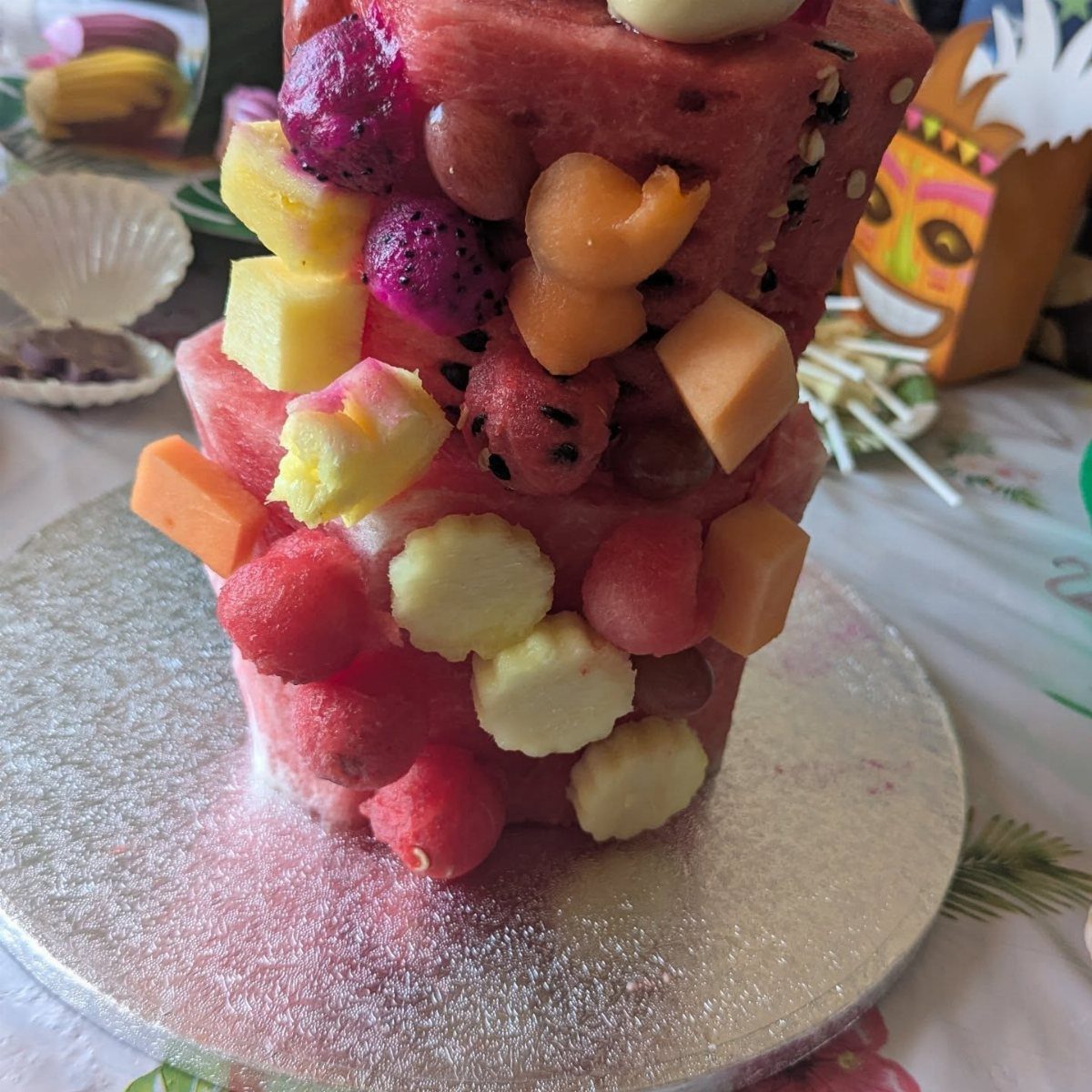 A colorful fruit sculpture made of watermelon and tropical fruits on a silver platter.