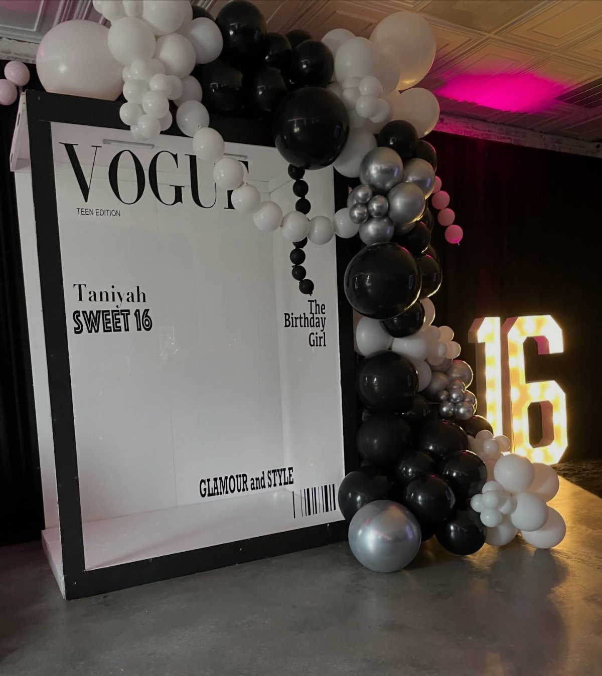 A large Vogue magazine photo booth frame decorated with black, white, and silver balloons.