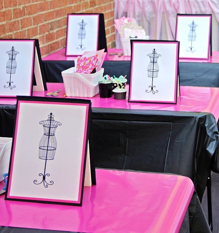 Framed mannequin drawings on pink and black tablecloth covered tables at a party.