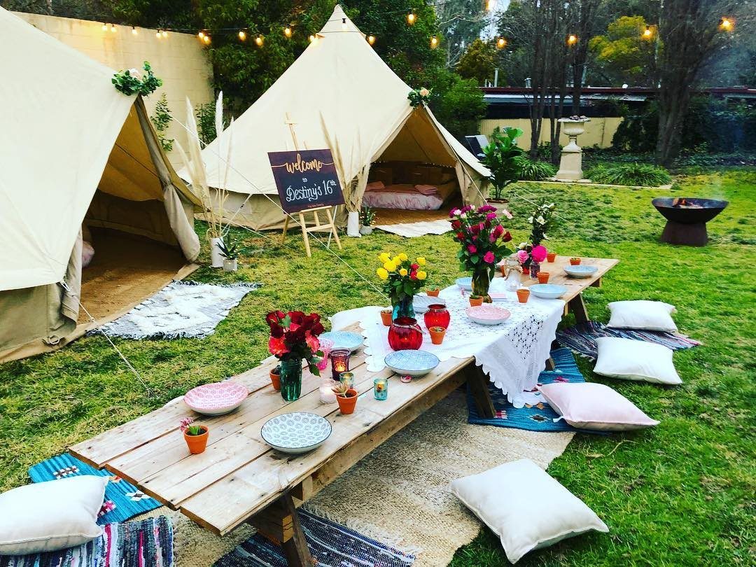 A decorated outdoor dining table and bell tents set up on a green lawn.