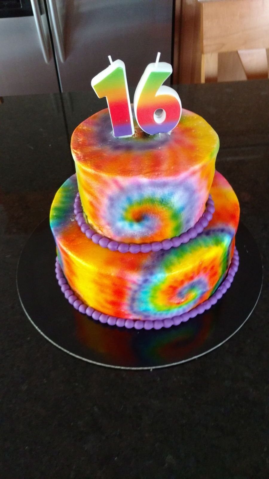 A two-tier rainbow tie-dye cake topped with large number 16 candles.