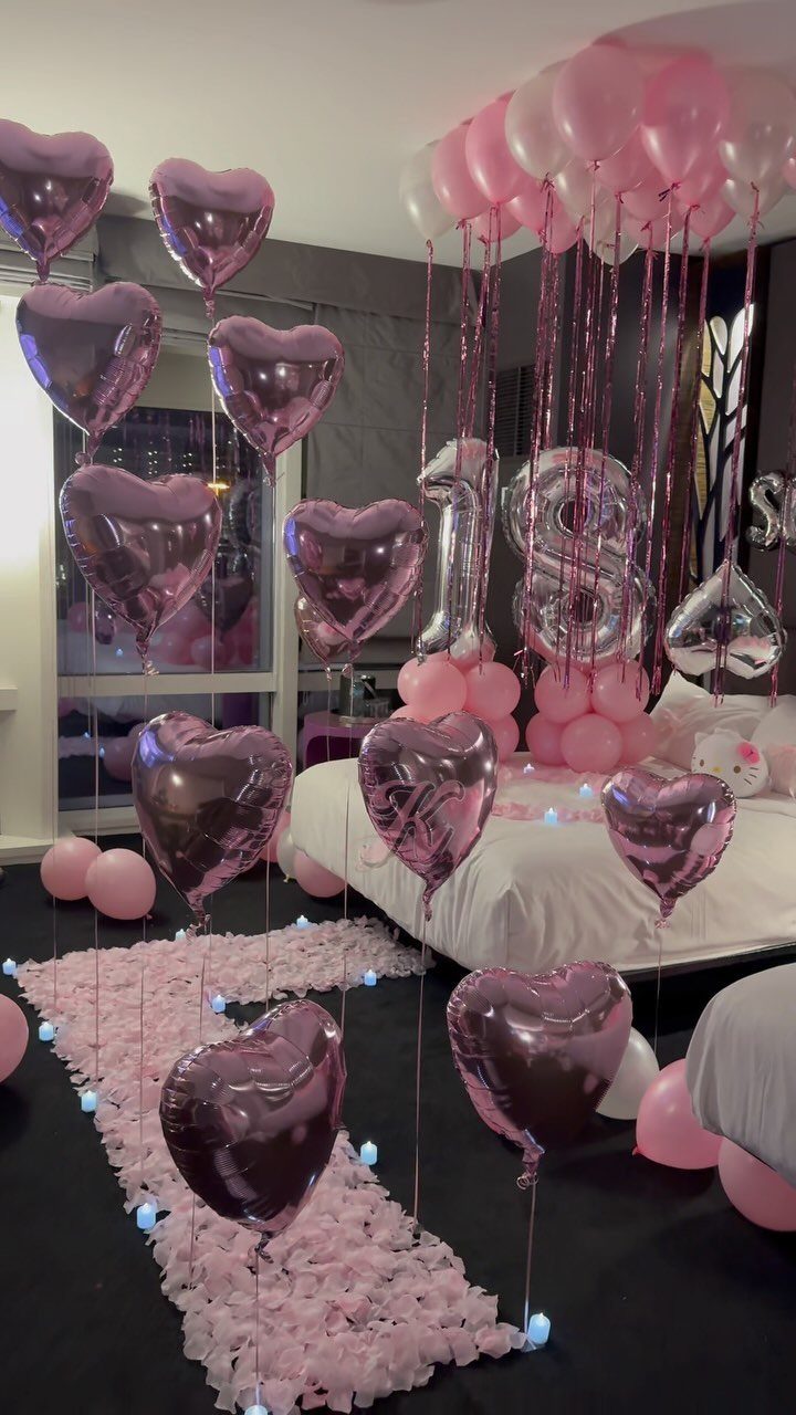 Pink heart balloons and silver eighteen balloons decorate a bed with rose petals.
