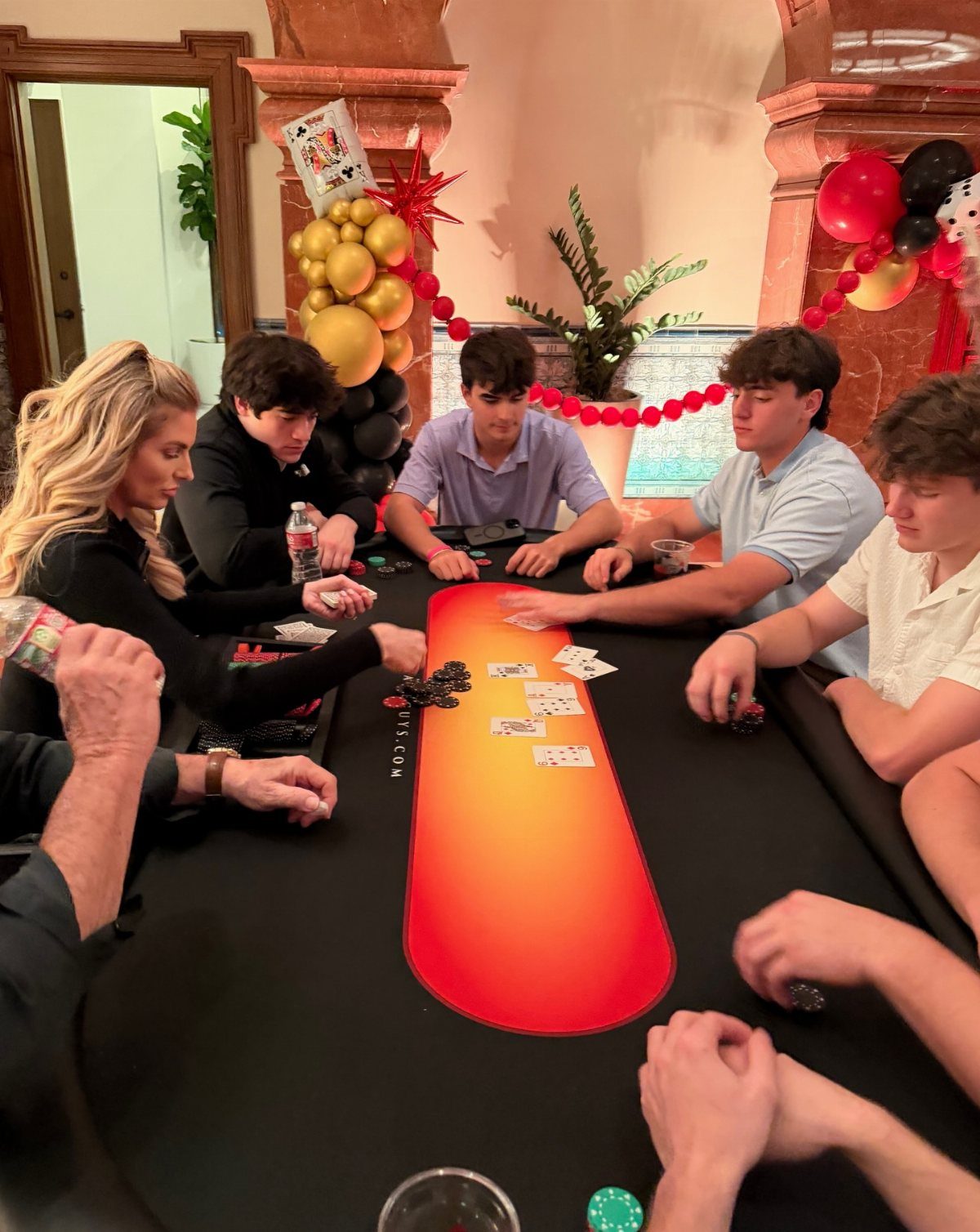 Young adults playing a card game with poker chips around a casino table.