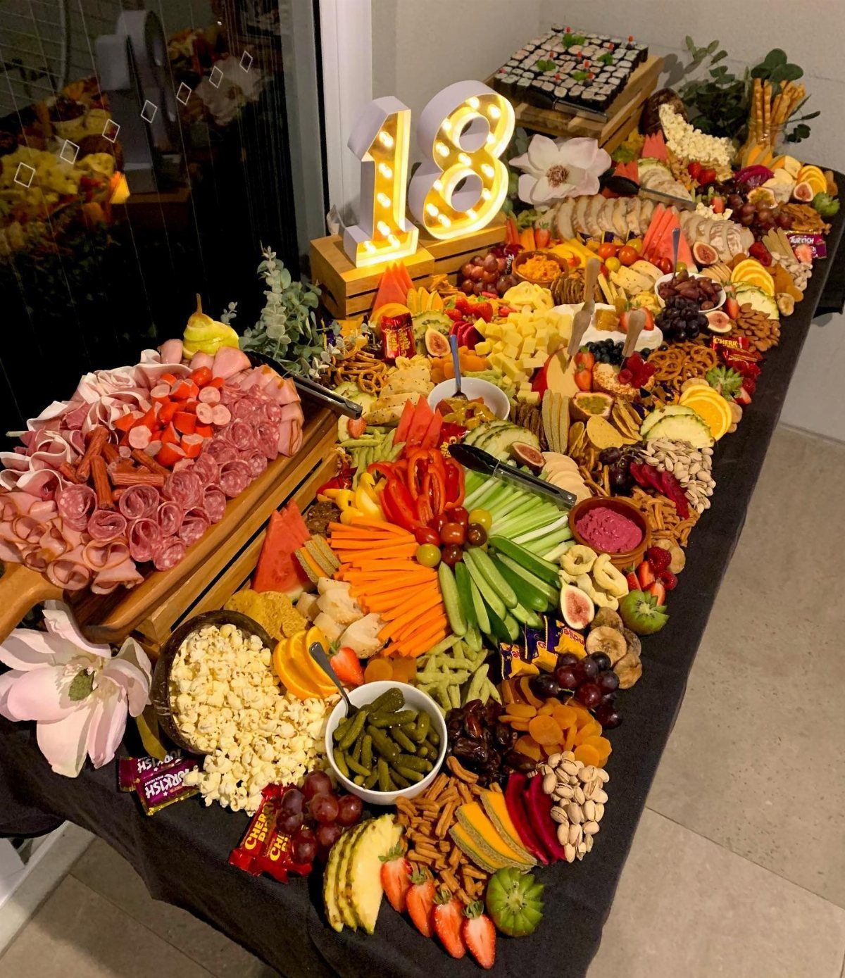 A large grazing table filled with various meats, cheeses, fruits, and vegetables with glowing eighteen numbers.