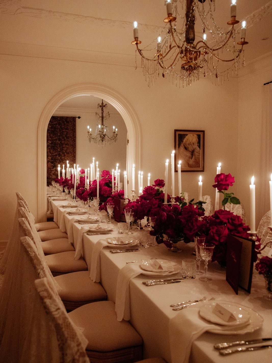 A long formal dining table decorated with pink flowers and many white taper candles.
