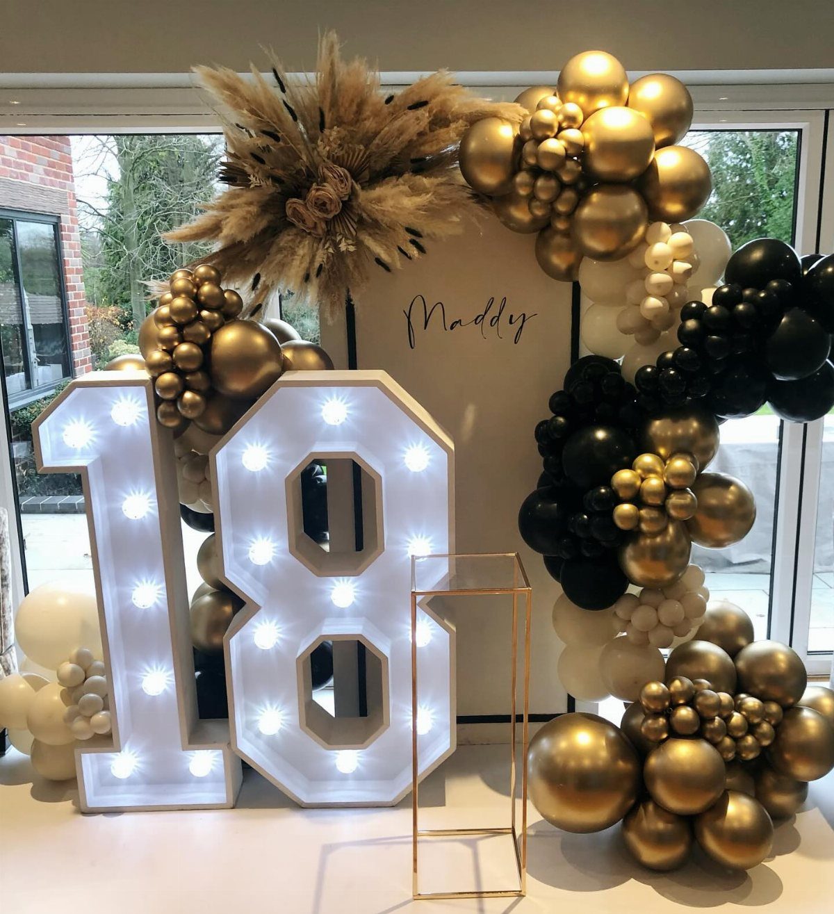 Large illuminated number 18 marquee lights surrounded by gold and black balloon decor.