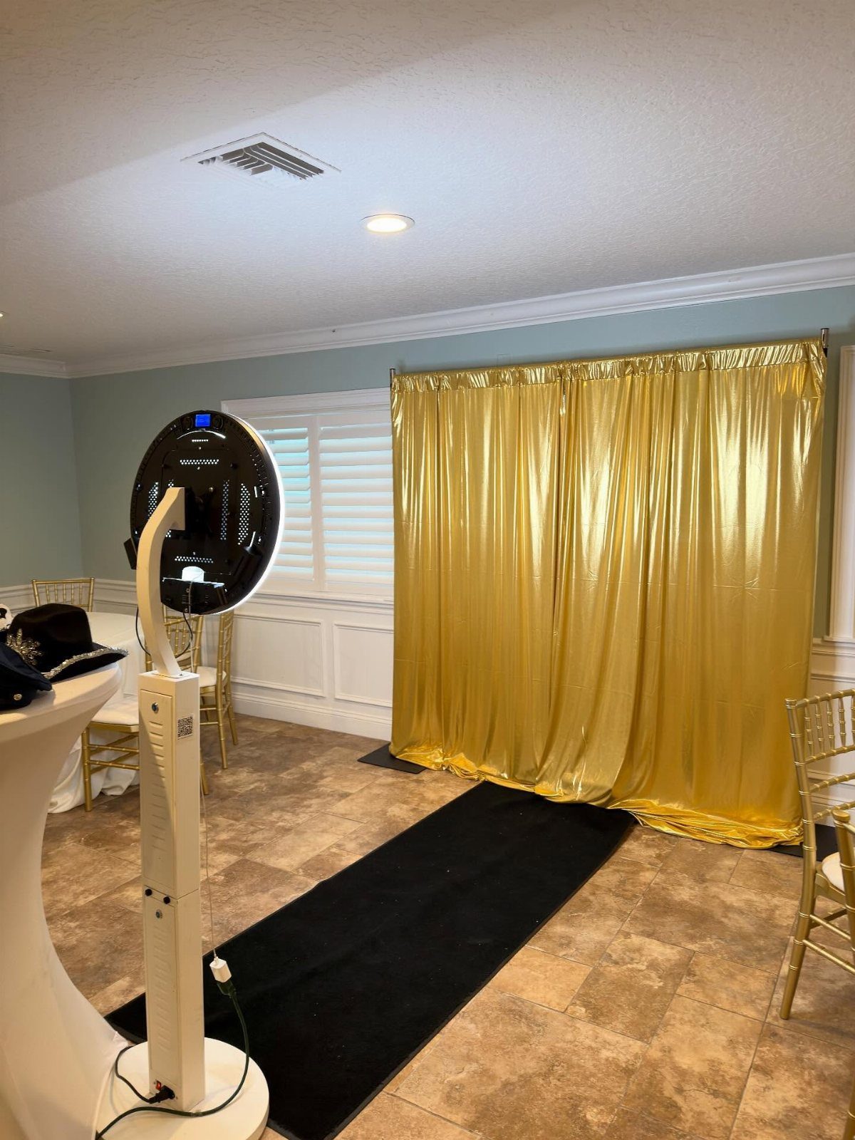 A professional photo booth setup with a ring light, black runner, and gold curtain backdrop.
