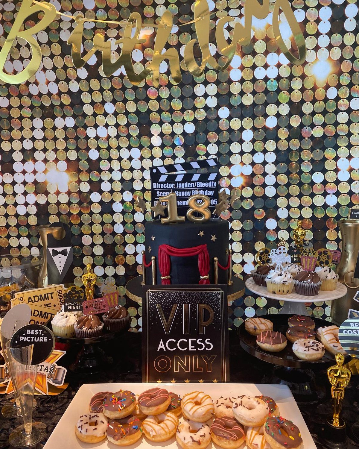 A Hollywood themed dessert table with a movie clapperboard cake and gold trophies.