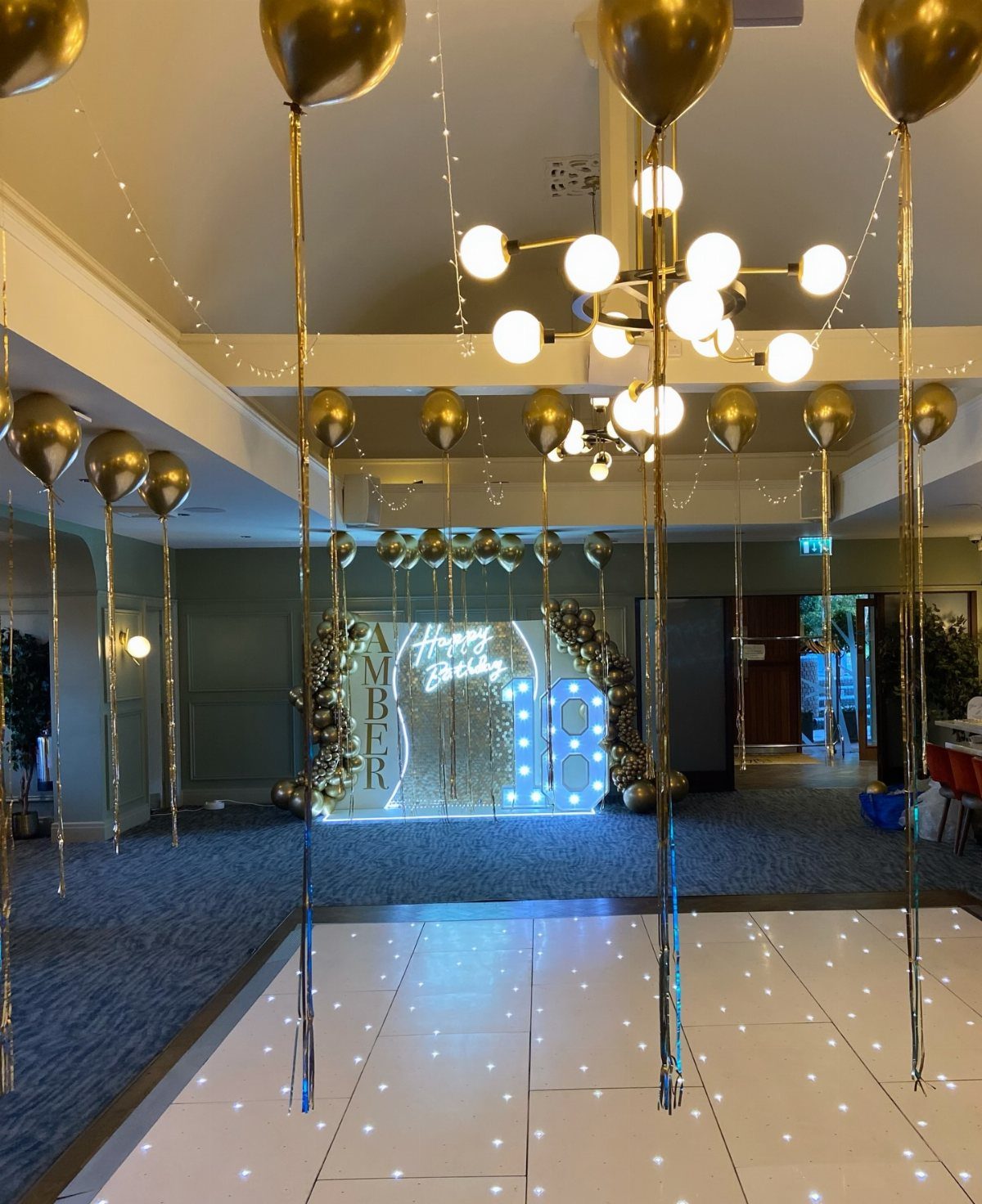 Gold balloons and a starlit dance floor in a decorated event hall.