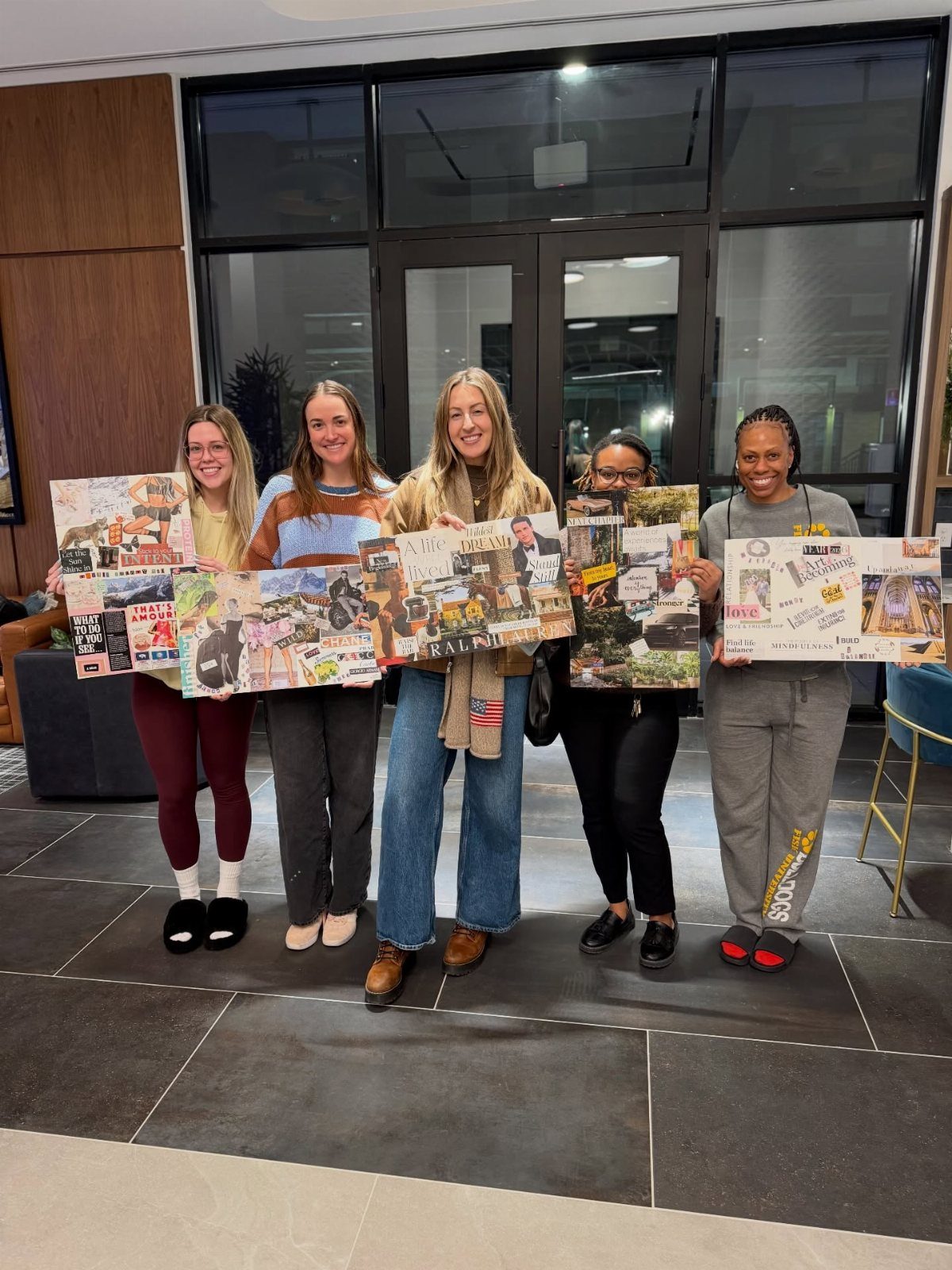 Five young women smiling while holding up their completed handmade vision board collages.
