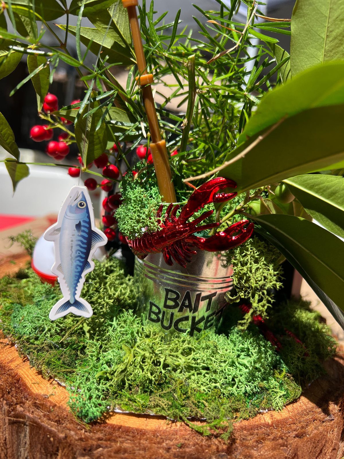 Fishing themed centerpiece with a bait bucket, red lobster, and fish cutout on green moss.