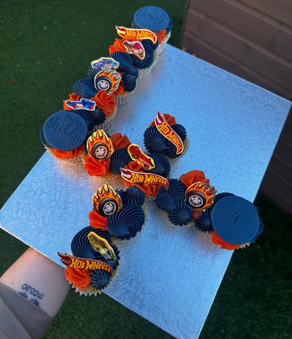 Hot Wheels themed cupcakes arranged in the shape of the number one on a silver board.