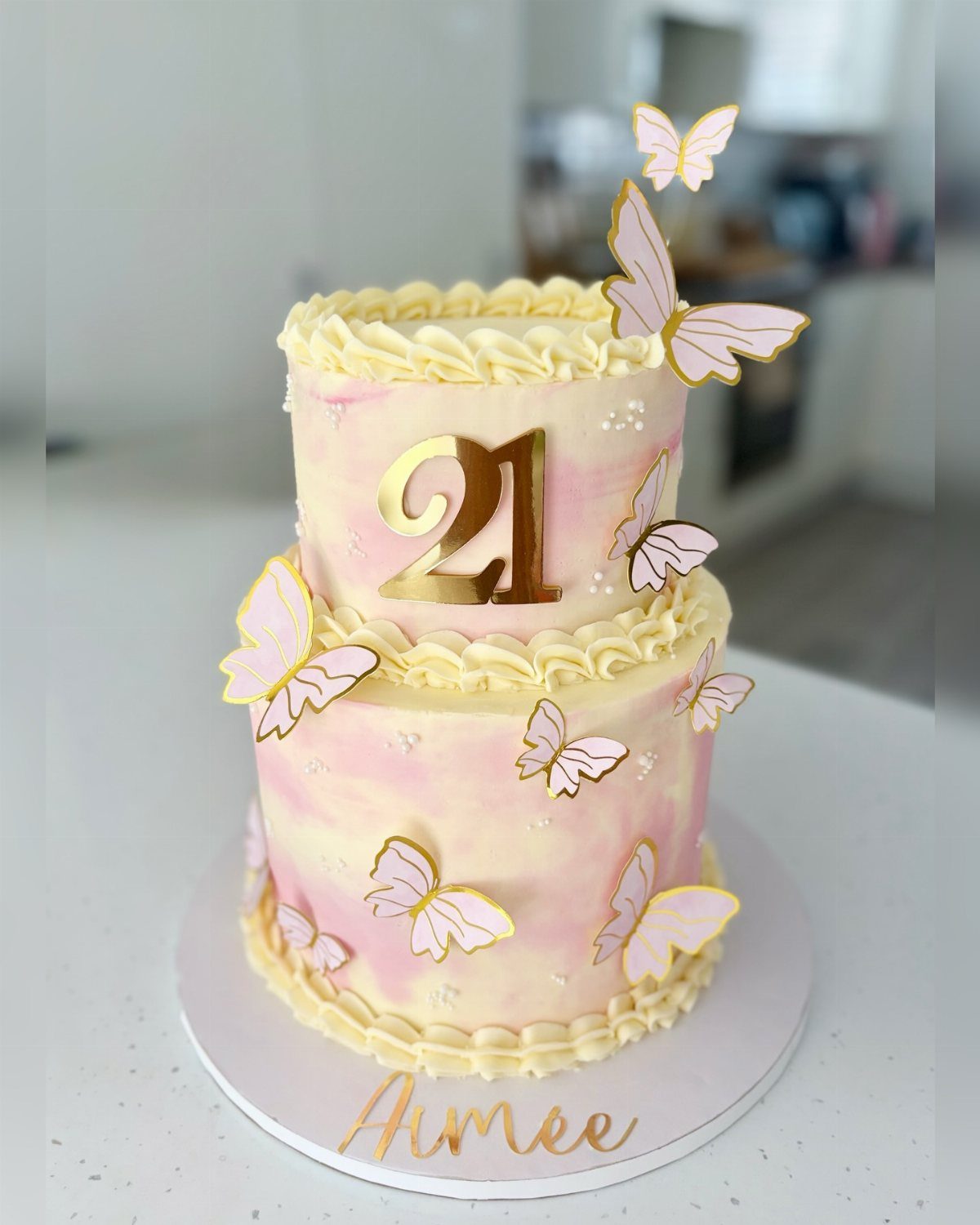 Two-tiered cake with gold butterflies and a '21' decoration.
