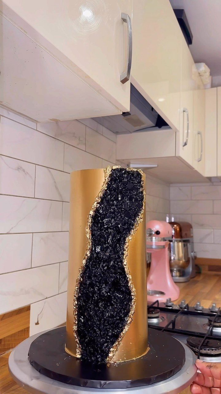 Elegant black and gold cake with a modern design in a kitchen.