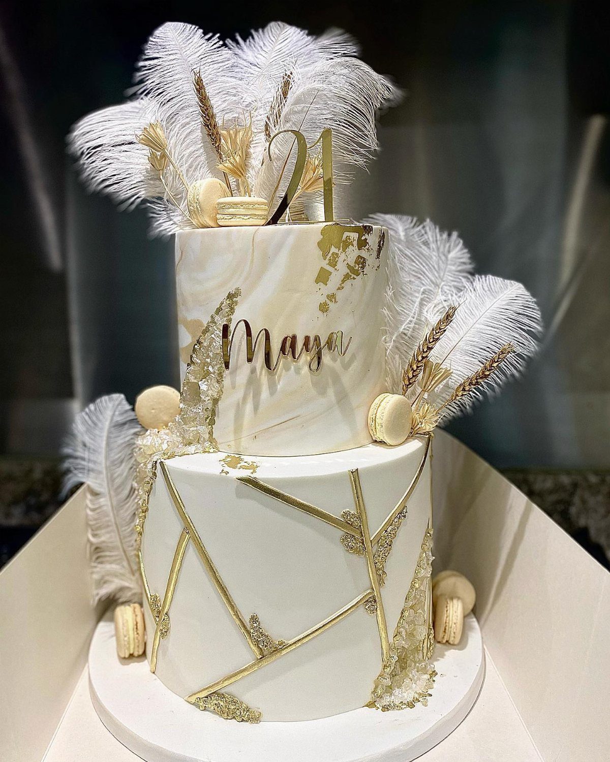 Elegant white and gold cake with feathers and macarons.