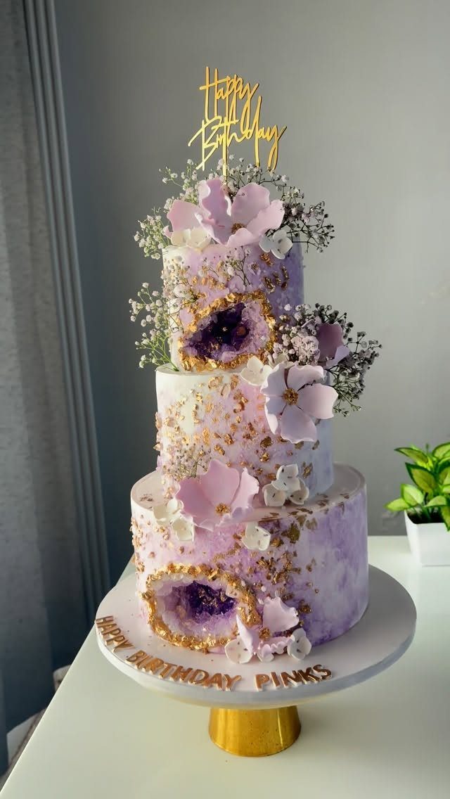 Three-tiered marbled purple cake decorated with gold leaf, edible flowers, and geode sugar crystals.