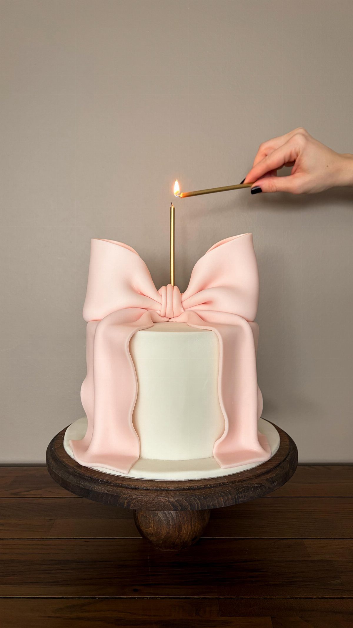 Minimalist white cake topped with a large pink bow and a lit candle.