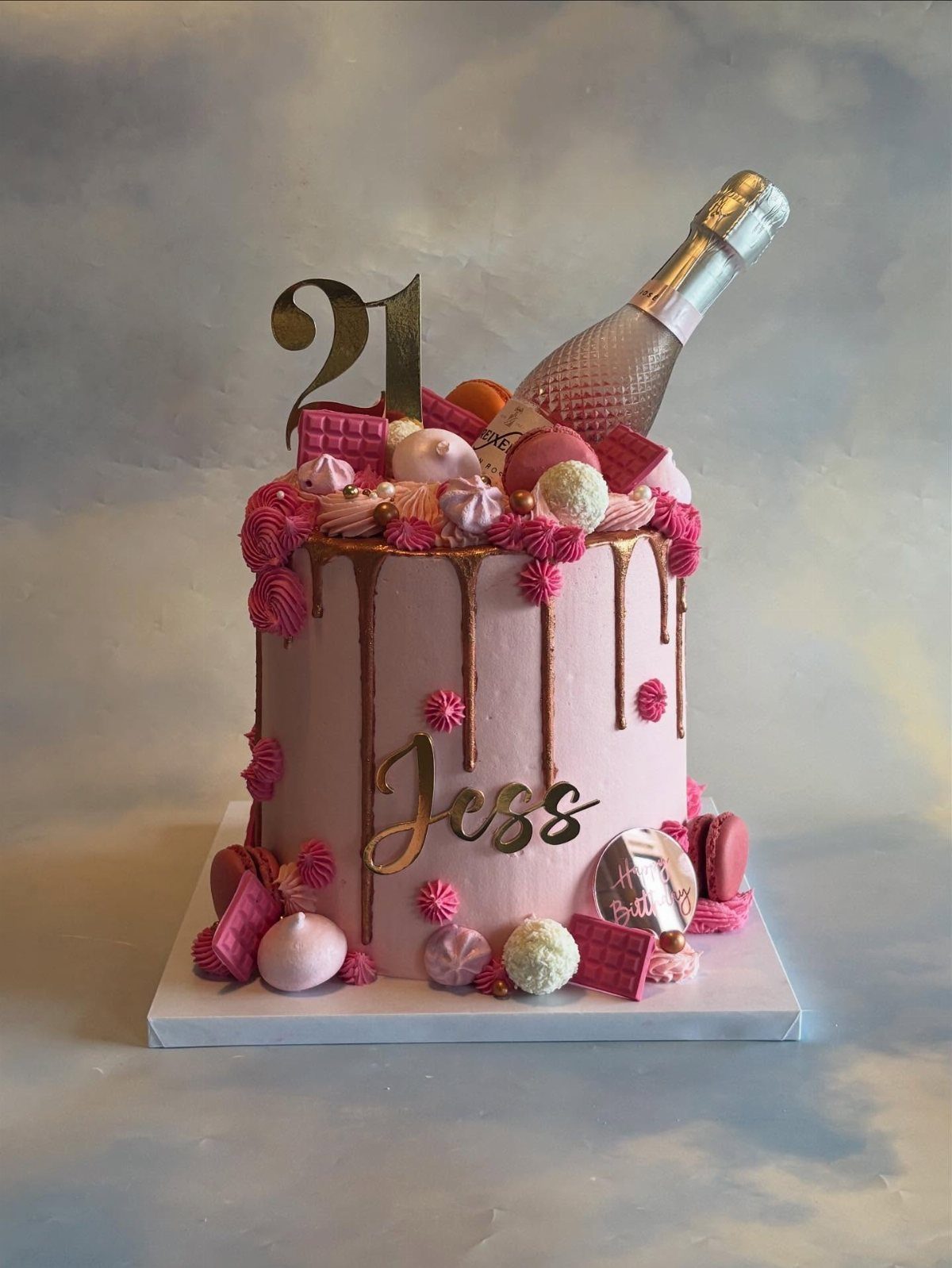 Pink drip cake with champagne, macarons, and the number 21.