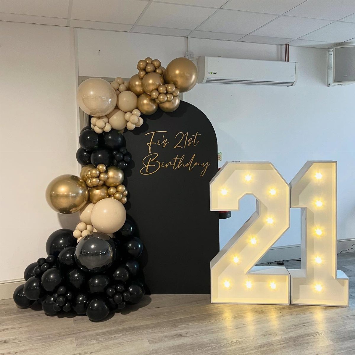 Balloon arch with black and gold balloons and illuminated '21' sign.