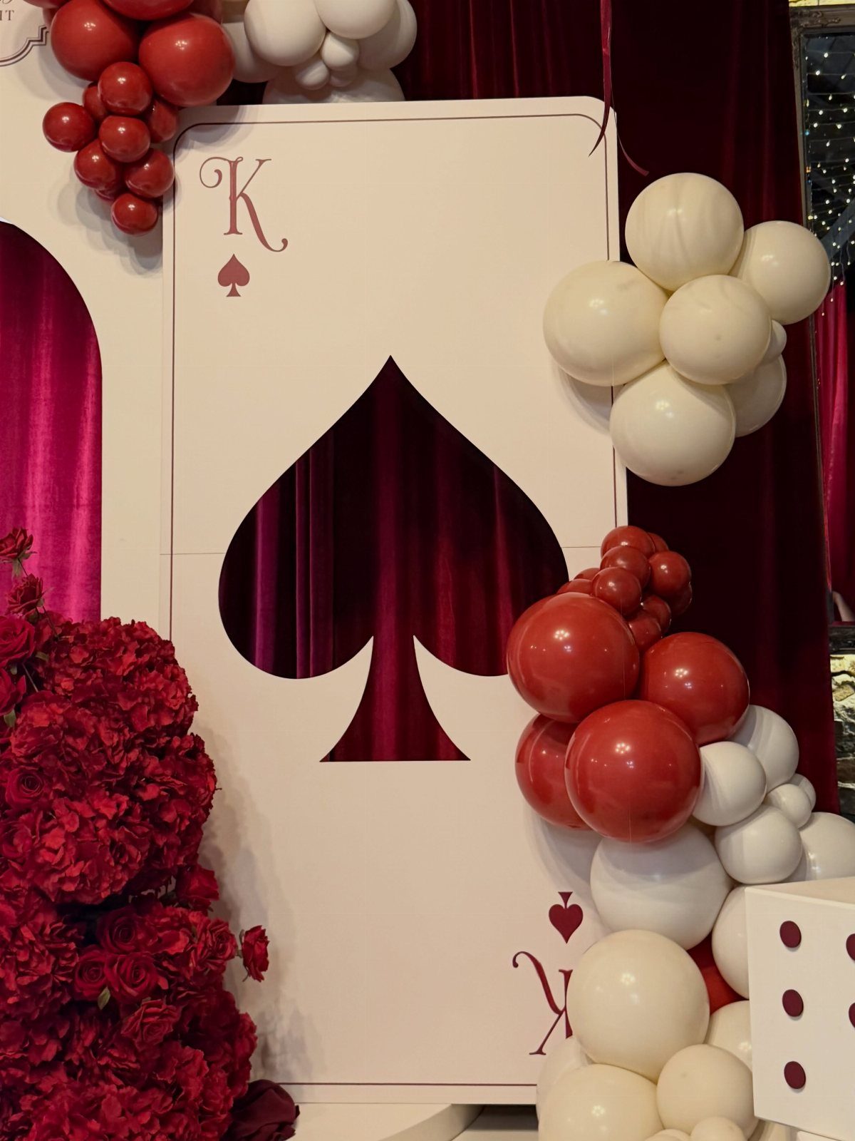 Large King of Spades playing card cutout surrounded by red and white balloon clusters.