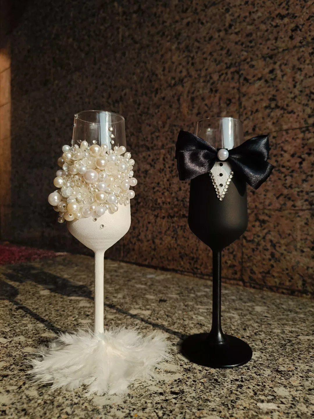 Two personalized champagne glasses, one with pearls and feathers, the other with a bow tie.
