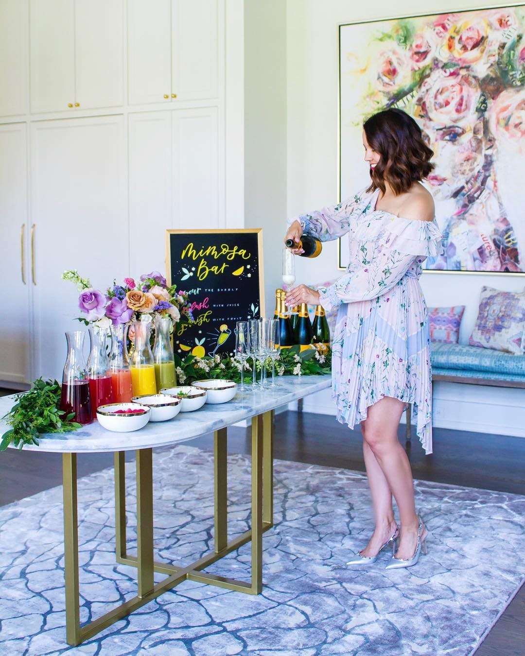 A woman pouring champagne at a colorful DIY mimosa bar.