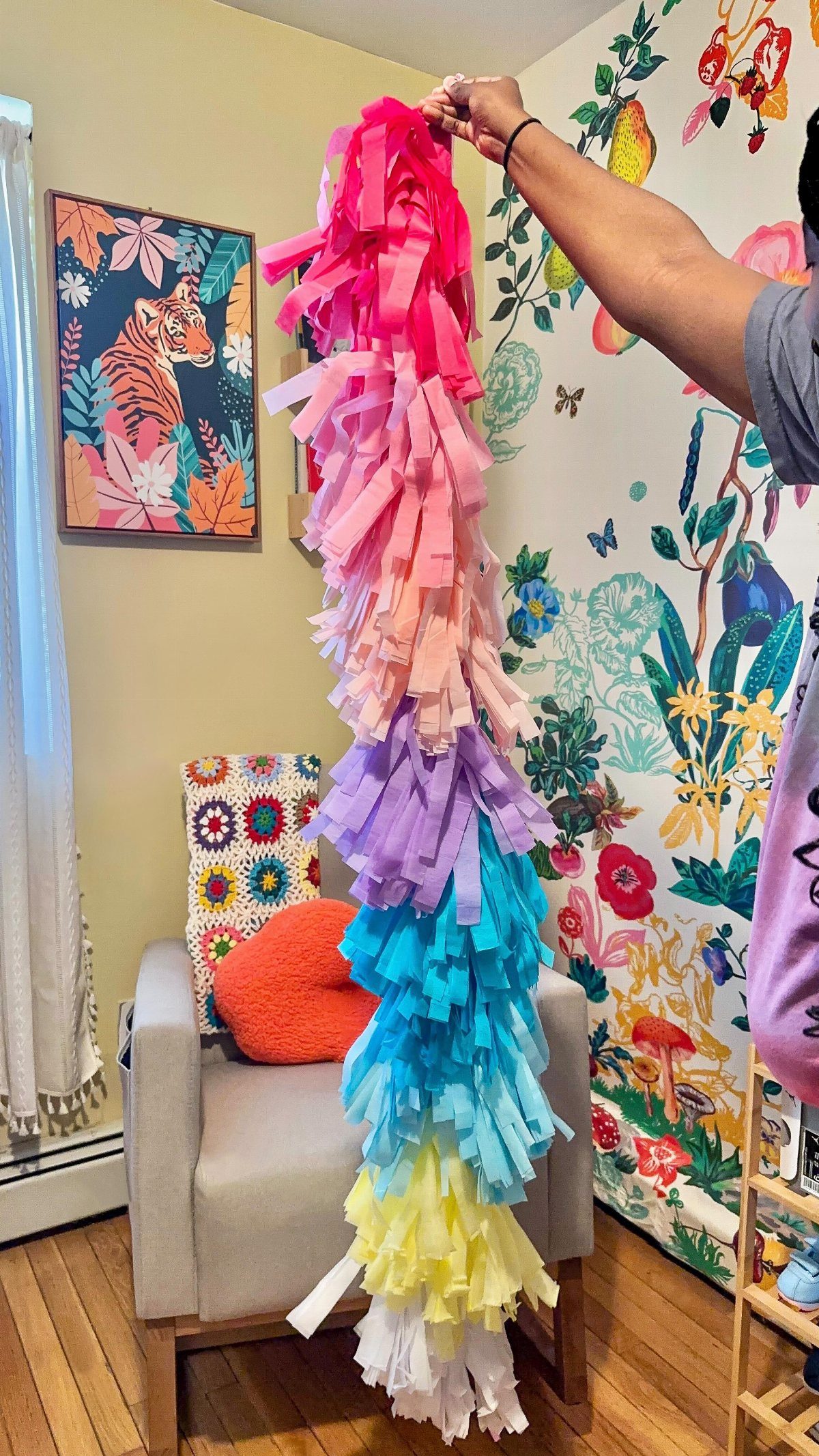 A colorful crepe paper fringe banner with rainbow-colored tassels being held up vertically.
