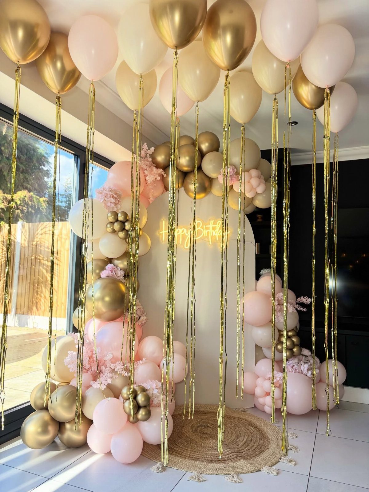 Balloon arch with pink and gold decorations for a birthday celebration.