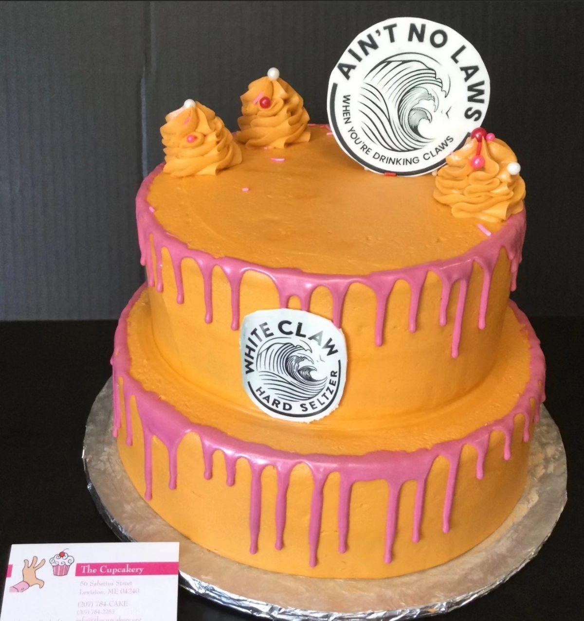 Two-tiered cake with orange frosting and White Claw logos.