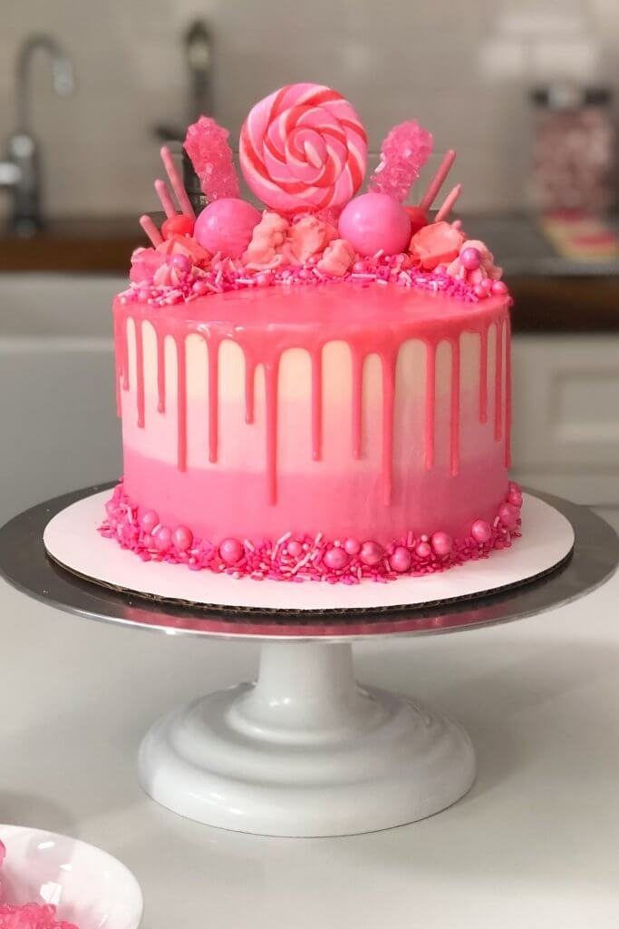 Colorful pink drip cake topped with candies and a lollipop.