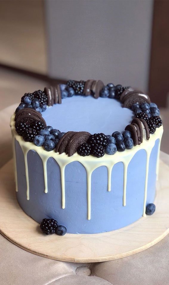 A light blue cake adorned with blackberries and Oreo cookies.