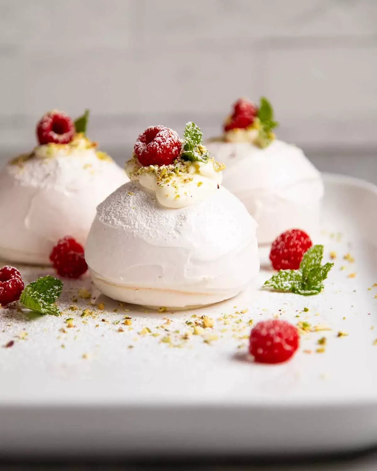 Three pavlovas topped with raspberries and mint on a white plate.