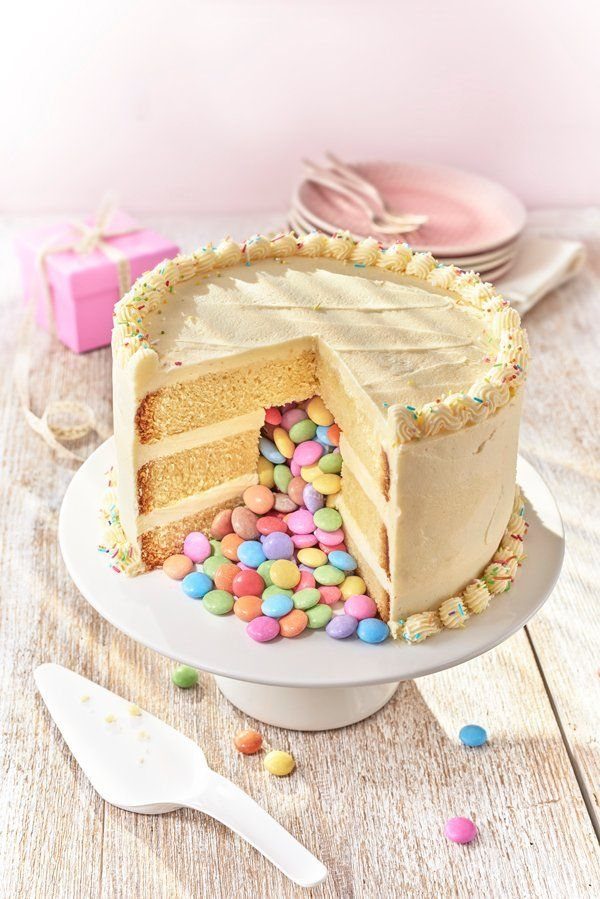 Piñata cake with candy spilling out, decorated with pastel frosting.