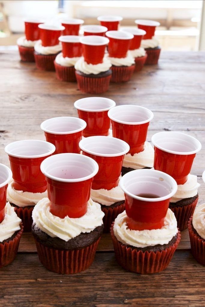 Chocolate cupcakes with white frosting and red plastic cups on top.