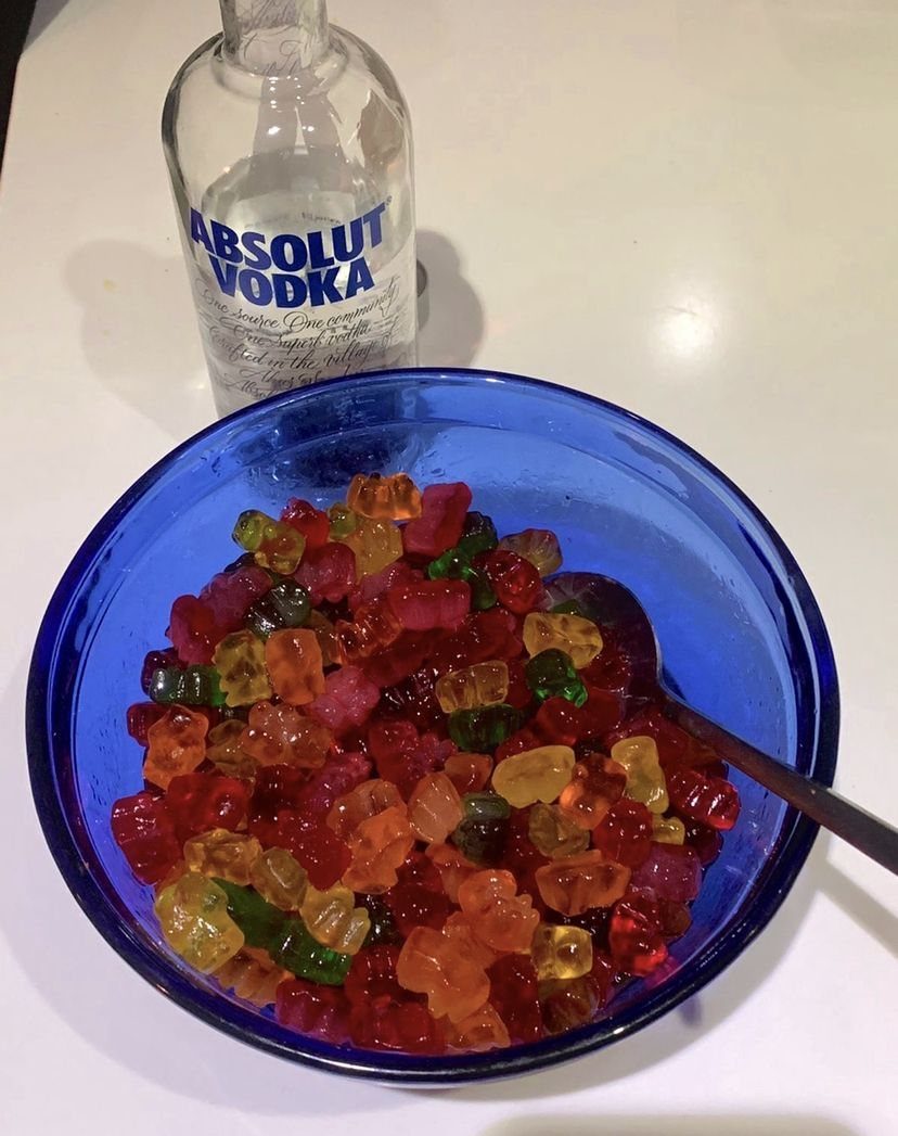 Colorful gummy bears in a blue bowl with a bottle of vodka.