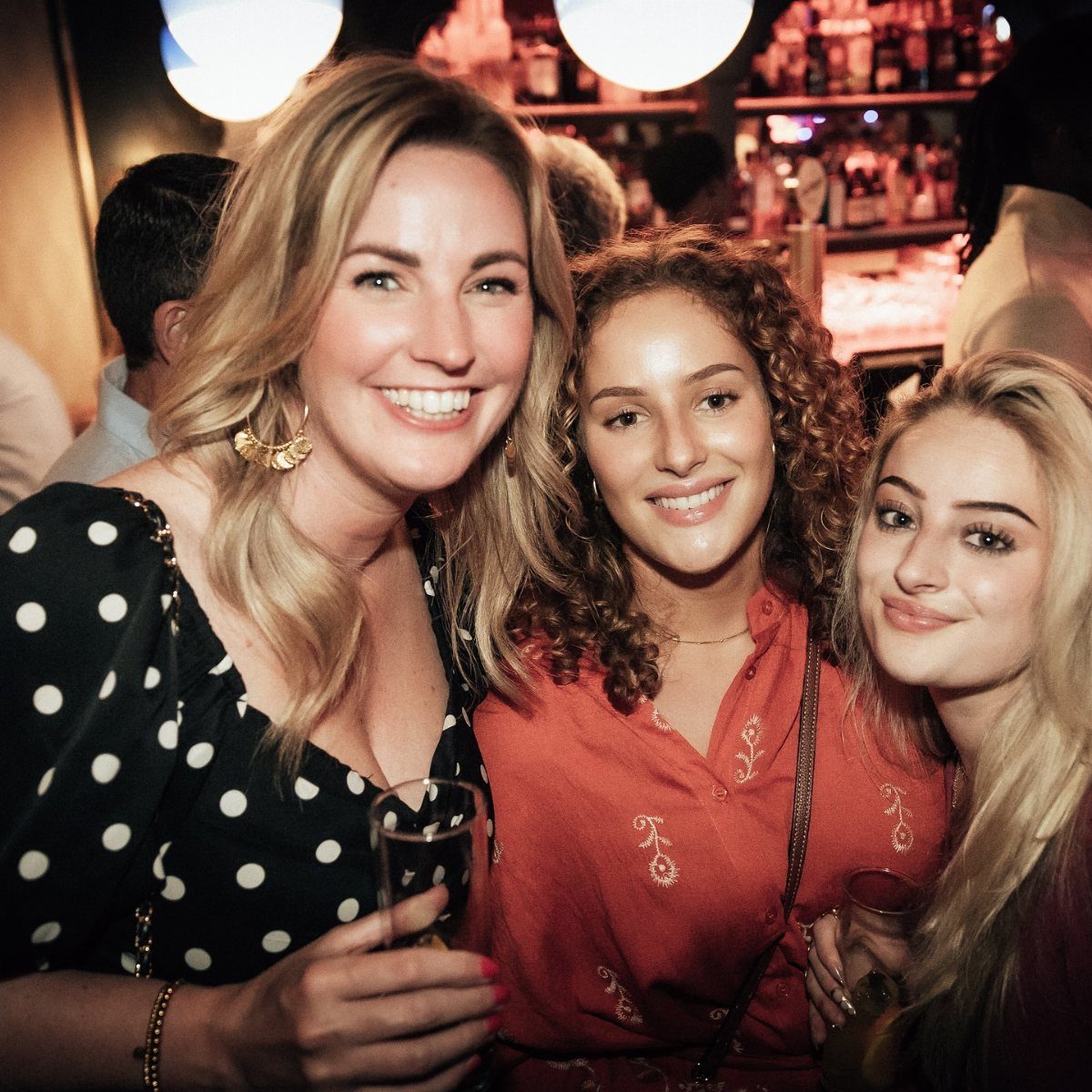 Three women enjoying drinks and smiling in a vibrant bar.