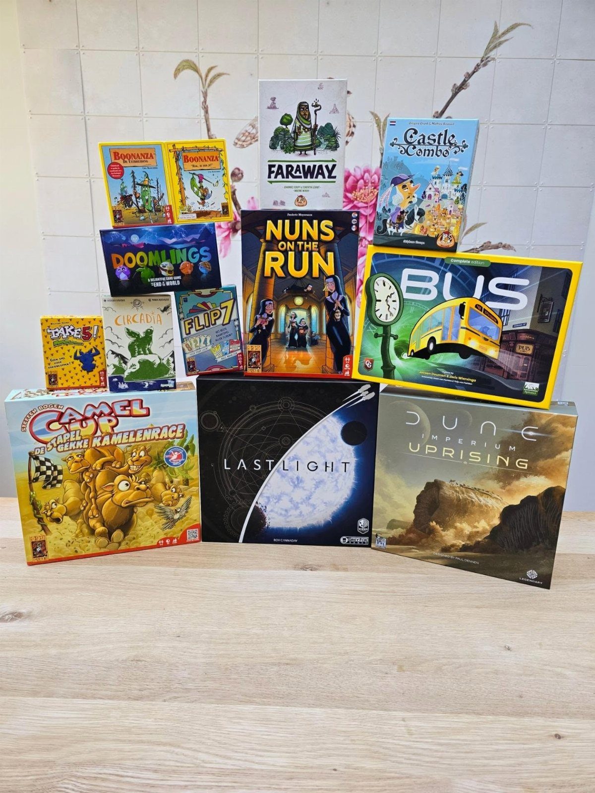 Various colorful board game boxes arranged on a wooden table against a tiled wall.