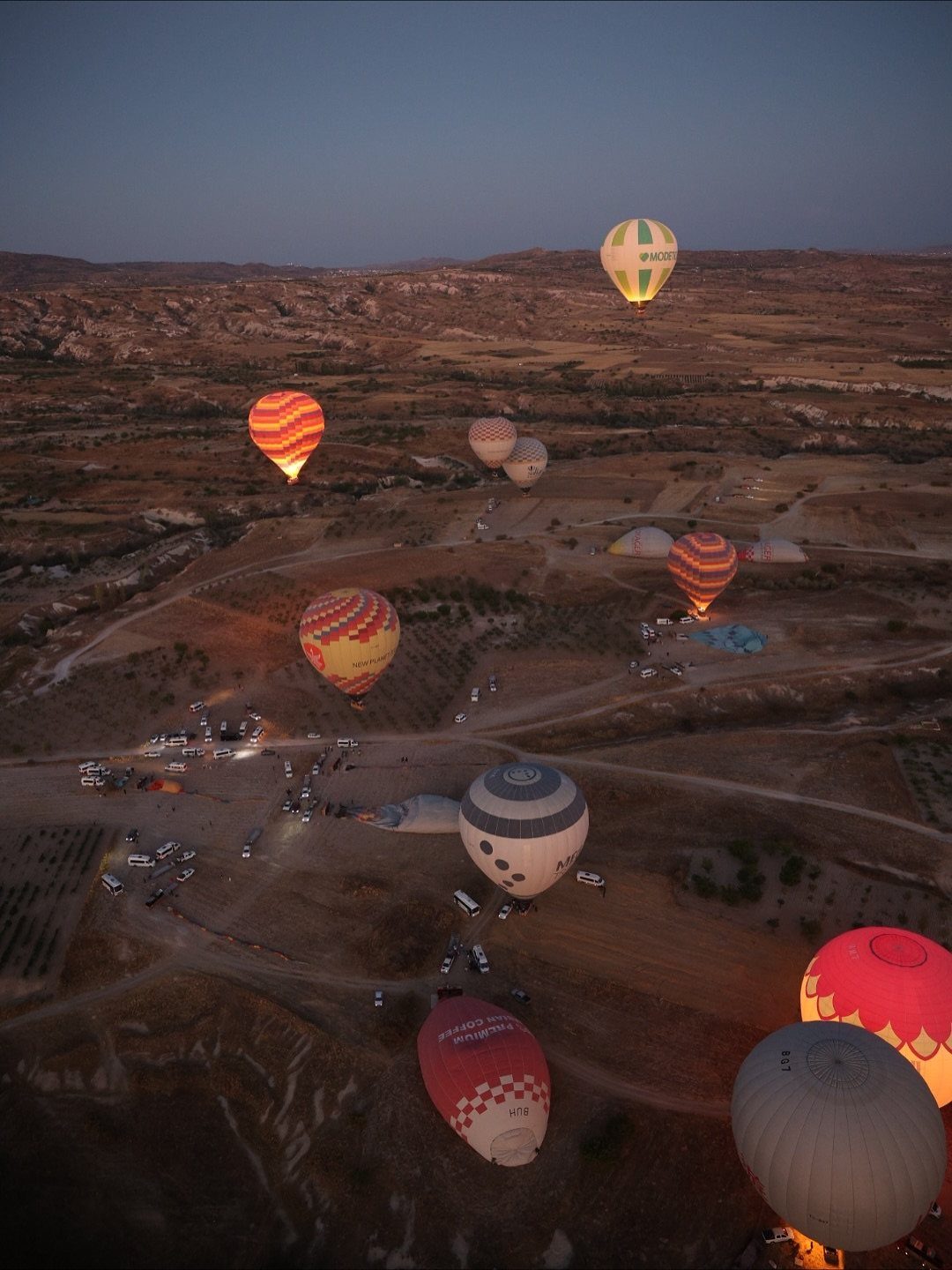 Colorful hot air balloons floating over a vast, rocky desert landscape during twilight.