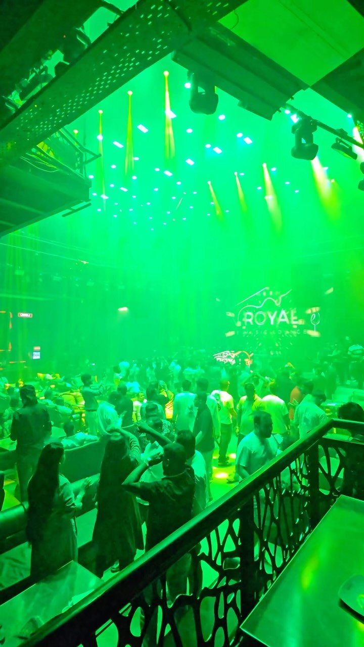 A crowded music lounge with green lighting and people dancing.